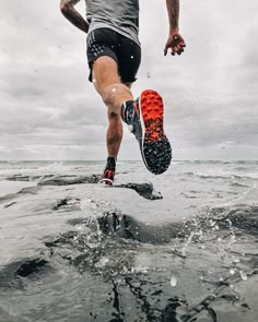 a man is running in the water with an orange shoe on his feet and black shorts