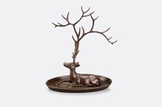 a bronze statue of a deer laying down on a plate with a tree in the middle