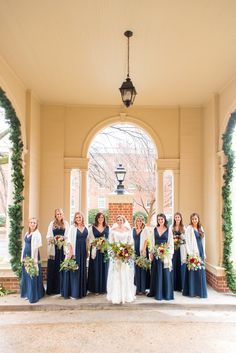 a group of women standing next to each other in front of a building holding bouquets