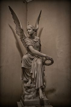 an angel statue sitting on top of a stone pedestal with wings above her head and holding a wreath