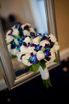 the bridal bouquet is sitting in front of a mirror with purple and white flowers