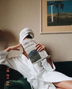 a person sitting on a couch with a towel wrapped around their head and reading a newspaper