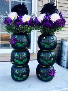 two black pumpkin vases with purple and white flowers sitting on top of each other