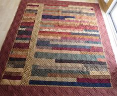 a large quilt is laying on the floor in front of a window with a wooden frame