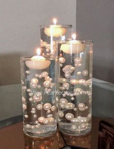 two glass vases filled with pearls and lit candles