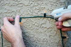 two hands are plugging wires into an electrical outlet on a stucco wall with lights