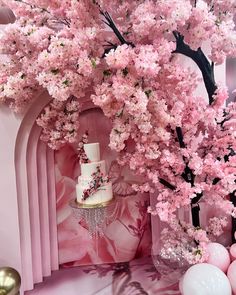 a cake sitting on top of a table next to pink balloons and cherry blossom trees