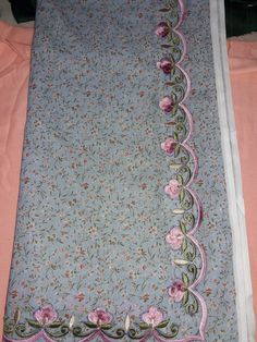 a blue blanket with pink flowers on it and a white border around the edges is laying on a bed