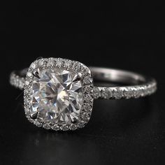 an engagement ring with a cushion cut diamond surrounded by pave diamonds on a black surface