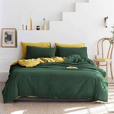 a bed with green sheets and yellow pillows in a white room next to some stairs