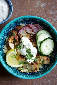 a blue bowl filled with meat and vegetables next to a cup of yogurt