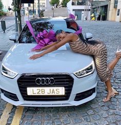 a woman leaning on the hood of a car with presents wrapped in pink ribbon and tied to it