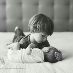 a little boy laying on top of a bed next to a baby