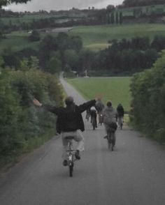 a group of people riding bikes down a road next to lush green fields and trees