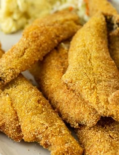 some fried food on a white plate with broccoli and mashed potatoes in the background