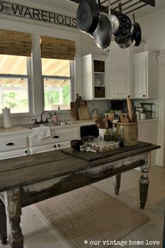 a kitchen with an old table in the middle and pots hanging from the ceiling above it