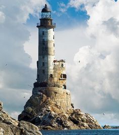 a large light house sitting on top of a rocky cliff next to the ocean under a cloudy blue sky