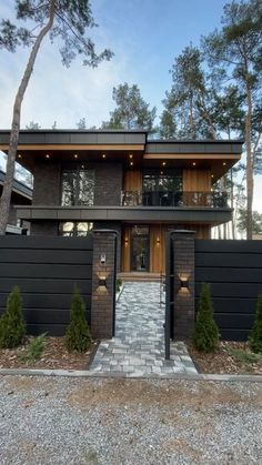 a modern house in the woods with stone walkway and brick pathway leading up to it's front door