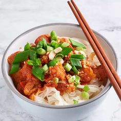 a white bowl filled with noodles and meat next to chopsticks on a marble surface