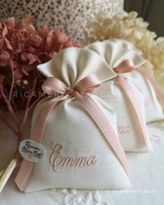 two small bags with pink ribbon and name on them sitting next to some white flowers