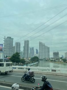 two motorcyclists are riding down the highway in front of some tall buildings