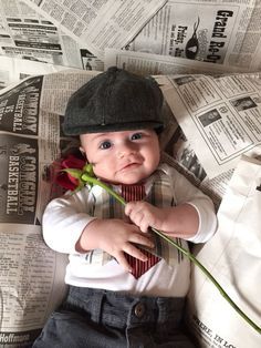 a baby boy laying on top of a bed holding a flower