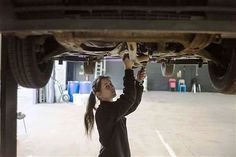 a woman is working on the underside of a car