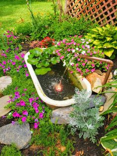 a garden filled with lots of flowers next to a small water fountain in the middle of a yard