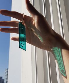 a person's hand holding onto a green keychain in front of a window