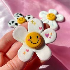 a hand holding a flower shaped brooch with smiley faces on it's petals