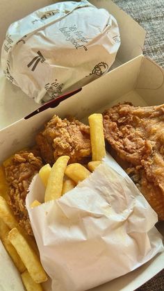 fried chicken and french fries in a takeout box with paper wrapper next to it