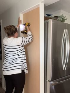 a woman is using a drill to paint the wall in her kitchen with a refrigerator