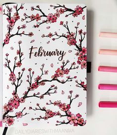 a pink and white notebook with cherry blossoms on it, next to markers that say february