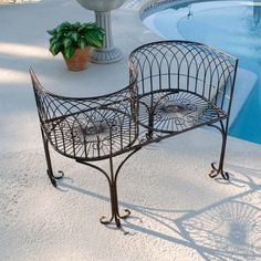 a wrought iron bench sitting next to a pool with a potted plant on it