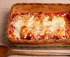 a casserole dish with cheese and sauce in it next to two wooden spoons