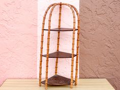 a three tiered bamboo shelf stands in front of a pink stucco wall and wooden floor