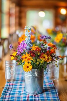 colorful flowers are in a metal bucket on a plaid table cloth at the end of a dining room table