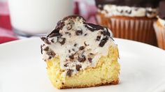 a cupcake with frosting and chocolate chips is on a plate next to a glass of milk