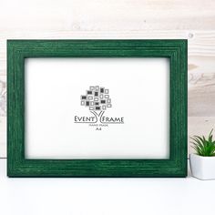 a green frame sitting on top of a white table next to a potted plant