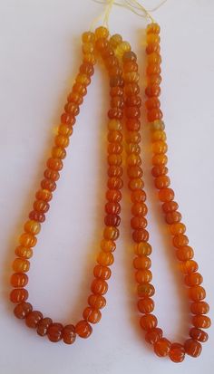 three orange beads are hanging from a string on a white surface, one is yellow and the other is brown