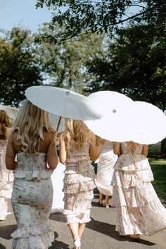 four bridesmaids walking down the road with umbrellas in their hands and dresses on