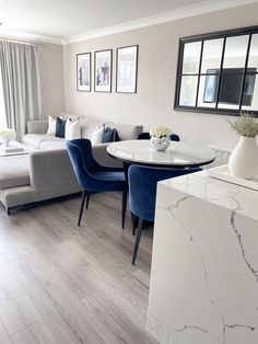 a living room filled with furniture next to a white table and blue chairs on top of a hard wood floor