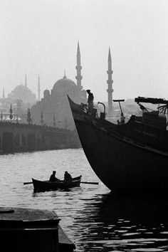 two people in a row boat on the water near a large building with domes and spires