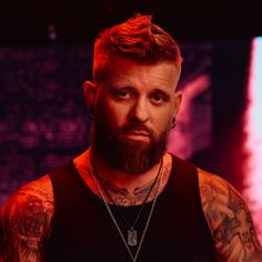 a bearded man with tattoos on his chest wearing a black tank top and looking at the camera