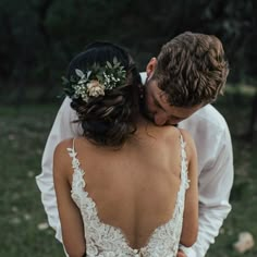 the bride and groom are standing close together in front of trees, grass and rocks