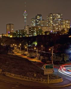 the city skyline is lit up at night with light trails on the road and street signs