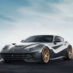 a silver sports car with gold rims parked in a parking lot next to the ocean