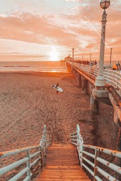 the sun is setting at the beach with people walking up and down the stairs to the water