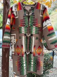 a coat hanging up on a clothes rack in front of a tree with autumn leaves