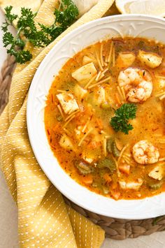 a white bowl filled with shrimp and pasta soup on top of a yellow towel next to bread